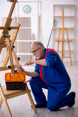 Naklejka na ściany i meble Old male carpenter repairing drawing easel