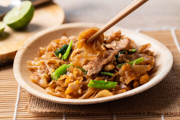 Thai food (Pad See Ew), Stir fried rice noodles with soy sauce, egg, kale and pork eating by use chopsticks