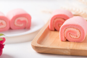 Pink strawberry roll cake or swiss roll with whipped cream and strawberry flavor on wooden plate