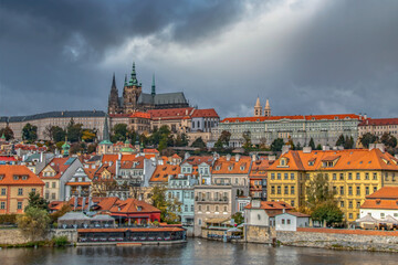 View of Prague in Czech Republic from Charles Bridge featuring Prague Castle, apartment buildings, shops and water, daytime, dark sky, nobody