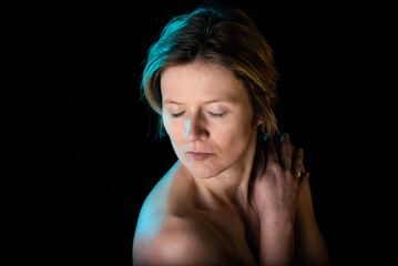 Low key studio portrait of a 35 year old white woman with naked chest, eyes closed