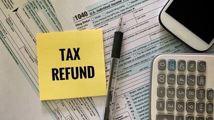 tax refund text on sticky note with 1040 tax form, pen and calculator and mobile phone background. Tax concept.
