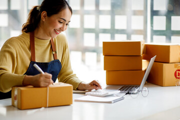 Startup SME small business entrepreneur, holding card box standing at her home office. Beautiful success Asian businesswoman online marketing, SME preparing package parcel delivery to her customer.