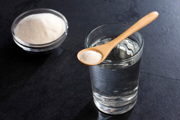 Powdered collagen protein in the spoon. Glass of water