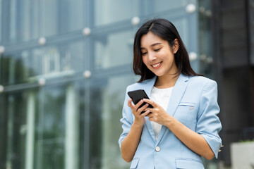Beautiful business woman using mobile phone to play social media in the buildings at downtown. Smart female using cell phone chatting for business communication. Smartphone concept.