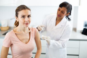 Obraz na płótnie Canvas Hispanic woman doctor vaccinating young caucasian woman patient.