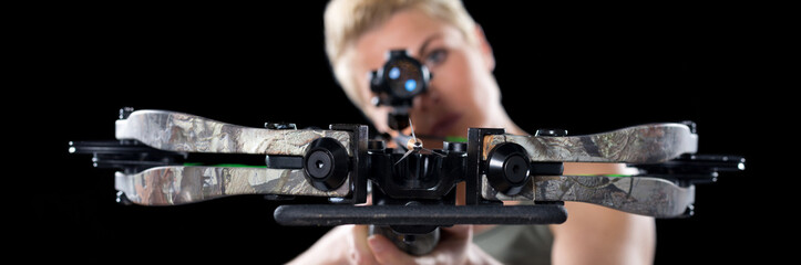 Young woman shooting with crossbow isolated on black background. - obrazy, fototapety, plakaty