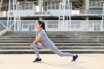 Healthy and fit asian woman wearing sportswear warming up in the city at sunrise. Confident young female stretching leg outdoor. before Workout exercise in the morning. Healthy lifestyle concept.