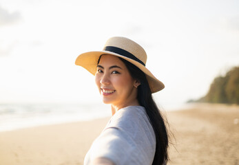 Follow me. Beautiful Asian woman holding hand husband walk around the beach while the sun set. Chilling moment travel in the holiday weekend. Asian Female with hat relax on the beach at summertime.