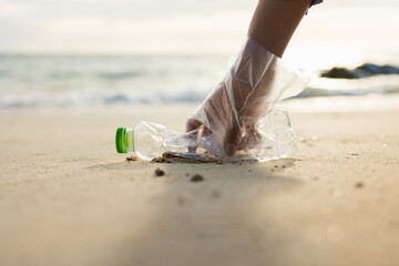 Close up woman hand pick up the plastic bottle on the beach. Female Volunteer clean the trash on...
