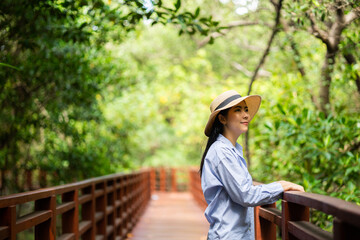 Fototapeta premium Young asian woman travel in the middle of nature with sunlight. Traveller blogger in mangrove forest. Rest on vacation holiday weekend. Beautiful female with hat and blue shirt walking in forest