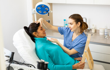 Skilled female beautician giving consultation to woman patient with mirror in aesthetic clinic
