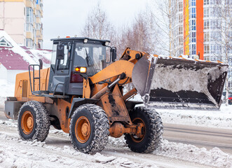 Big orange tractor cleans up snow from the road and loads it into the truck. Cleaning and cleaning...