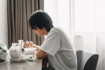 Asian young man is eating unhealthy takeaway food in the room 