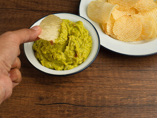 A bowl with fresh guacamole and potatoes chips on a white plate over a wooden table