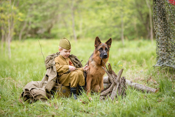 a boy in a military uniform in a clearing, sitting by a campfire with a German shepherd.Two friends defend the motherland