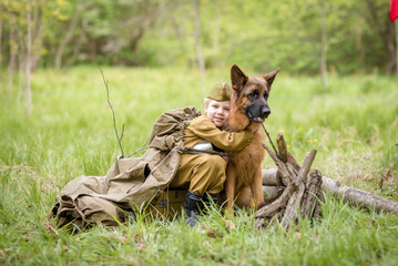 a boy in a military uniform in a clearing, sitting by a campfire with a German shepherd.Two friends...