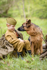 a boy in a military uniform in a clearing, sitting by a campfire with a German shepherd.Two friends...