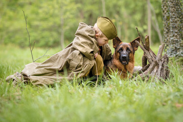 a boy in a military uniform in a clearing, sitting by a campfire with a German shepherd.Two friends...