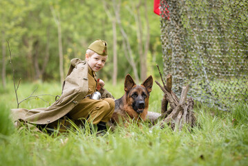 a boy in a military uniform in a clearing, sitting by a campfire with a German shepherd.Two friends...