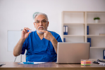 Old male doctor holding thermometer in the clinic