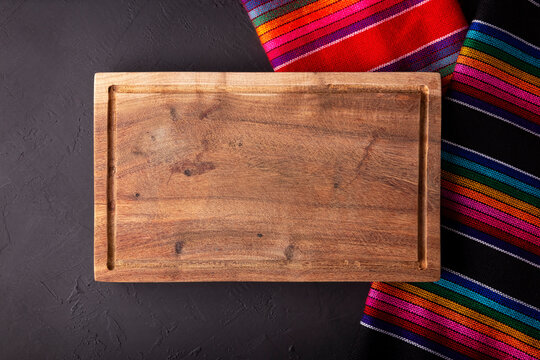 Wooden Cutting Board on colorful traditional mexican fabric, Copy space. Flat lay image