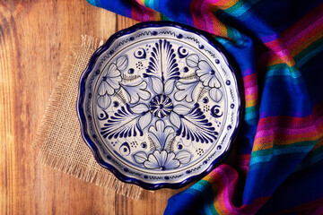 Mexican Cuisine Background, colorful traditional fabric and empty talavera style plate on wooden rustic table. Flat lay