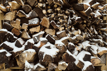 frontal view of differently sized stacked fire wood partially covered with snow