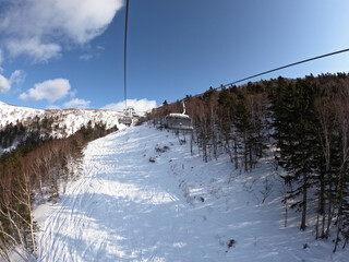 A cable car that transports skiers and snowboarders on a winter slope. On a sunny winter day in a ski resort, the lift goes up, carries people, top view from a chair lift on a snowy background.