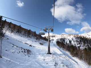 A cable car that transports skiers and snowboarders on a winter slope. On a sunny winter day in a ski resort, the lift goes up, carries people, top view from a chair lift on a snowy background.