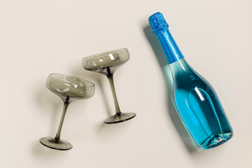 Champagne glasses tinted grey glass, Blue Champagne or blue sparkling wine bottle. Light Festive drink concept, glare and sunlight. Modern wine colored glasses. Creative flat lay