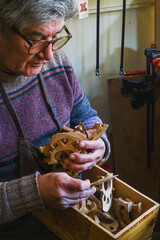 hispanic senior luthier classic instrument maker in his workshop looking for the right bridge in a...