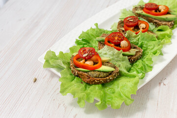 Vegan breakfast. Dietary nutrition. Sandwiches of grain bread with vegetables and nuts on a white plate on a white wooden table. Side view, close-up, space for text.
