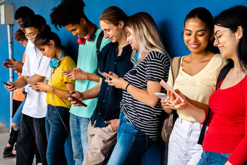 Happy and smiling group of multiracial high school students using cellphone standing against blue wall. Social media.