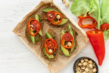 Vegan sandwiches with peppers, avocados, spicy spinach sauce and grain bread on a wooden tray and ingredients nearby. View from above. a light healthy snack. Dietary nutrition. 