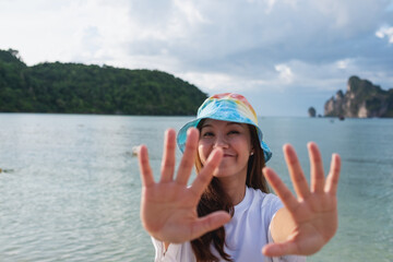 Portrait image of a happy young woman outstretched hand while strolling on the beach with the sea and blue sky background