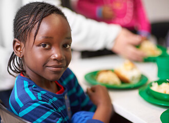 No child should be hungry. Portrait of a little girl sitting at a dining table with food provided by volunteers.