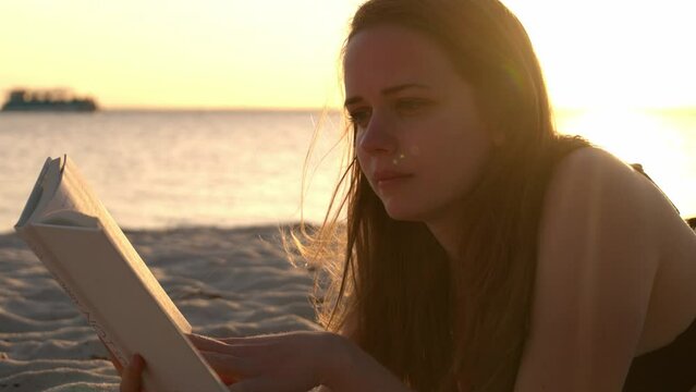 Young woman reads a book while lying on the beach at sunset - travel photography