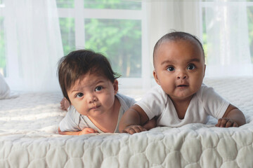 Two happy different skin color baby  4-5 months old crawling on white bed, and interact, and looking at someone