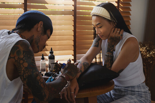 Tattoo artist doing tattoos for women, professional tattooer doing tattoo using tattoo machine in studio