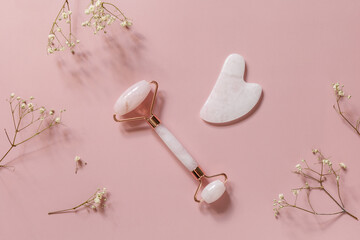Rose quartz facial massage roller over pink background with gypsophila flowers. Massage tools with...