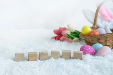 Easter eggs and rabbit ears in basket and blank wooden block on white fur