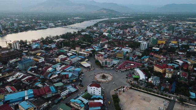 Large Durian Roundabout that several vehicles drive over in the densely populated city of Kampot with the high mountains in the background. High angle drone panning shot