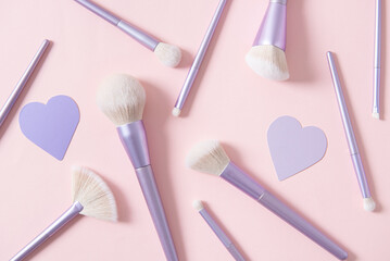 Different make up brushes, favourite make up tools on pink background with hearts. Professional make up brushes for visagist. Cosmetic composition. Magazine, cosmetics store background