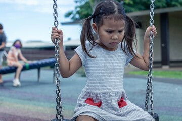 A sad little girl sitting alone at the playground with no friends. Bullying.