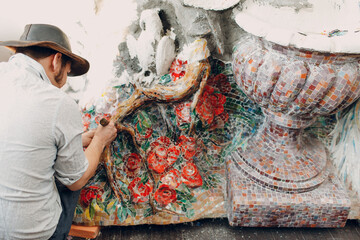 Man mosaics master in hat making smalt glass mosaic panel. Male mosaicist at work