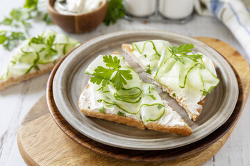 Healthy breakfast or holiday snacks. Toast with cucumbers, herbs and ricotta on a rustic wooden table.