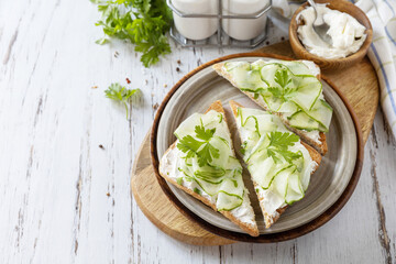 Healthy breakfast or holiday snacks. Toast with cucumbers, herbs and ricotta on a rustic wooden table. Copy space.