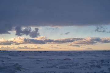 Fototapeta premium Iced. over Lake Michigan - Frozen Lake with snow, beautiful colorful sky, and clouds and sunset color sky in the background