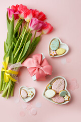 Happy Easter. Multi-colored pastel easter cookies gingerbread, gift box seasonal flowers tulips on pink background. Easter concept, copy space, flyer, banner, coupon, greeting card, invitation